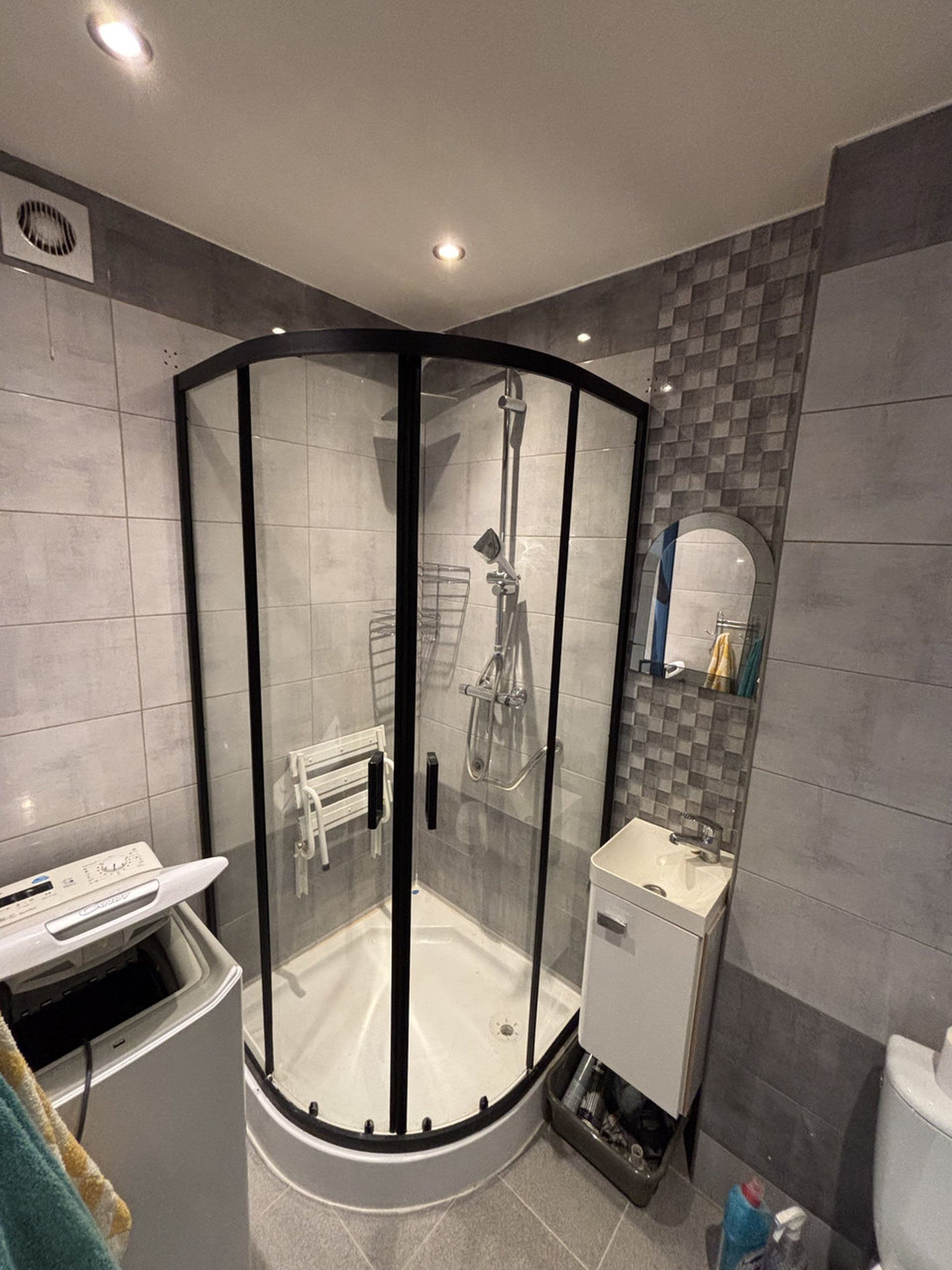 A modern bathroom with a glass-enclosed shower, a white sink, and a tiled backsplash.