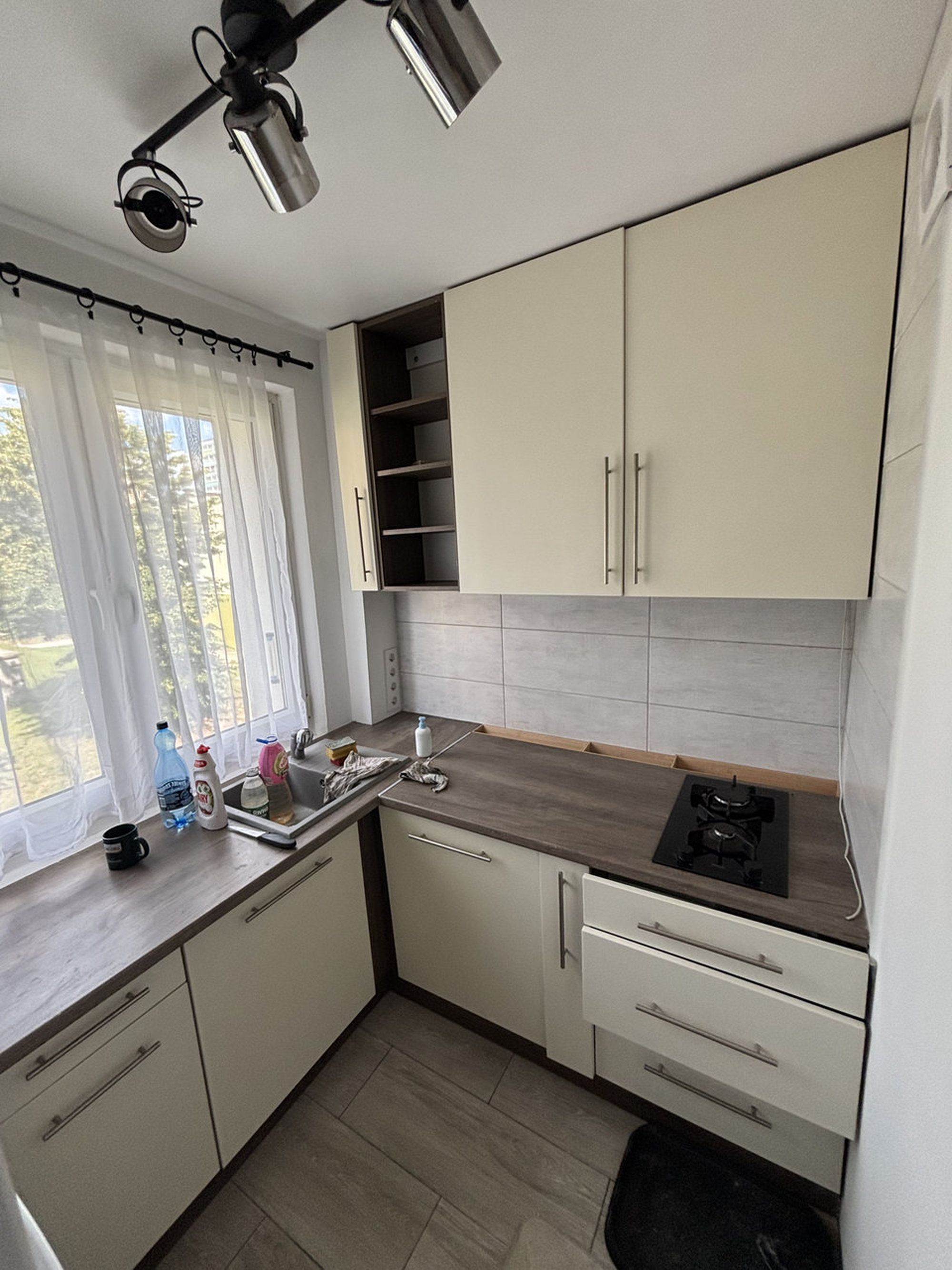 A compact kitchen with a window, a sink, a stove, and cabinets.