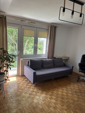 A room with a sofa, a potted plant, a desk, and a chair.