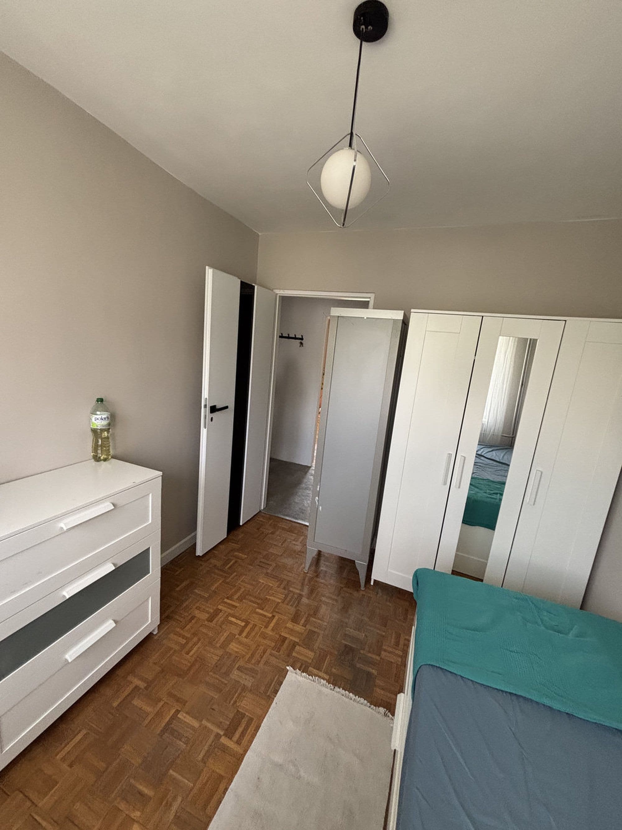 A bedroom with a bed, wardrobe, and a hanging light fixture.
