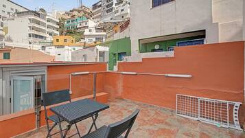 A rooftop terrace with a table and chairs, a metal railing, and a view of surrounding buildings.