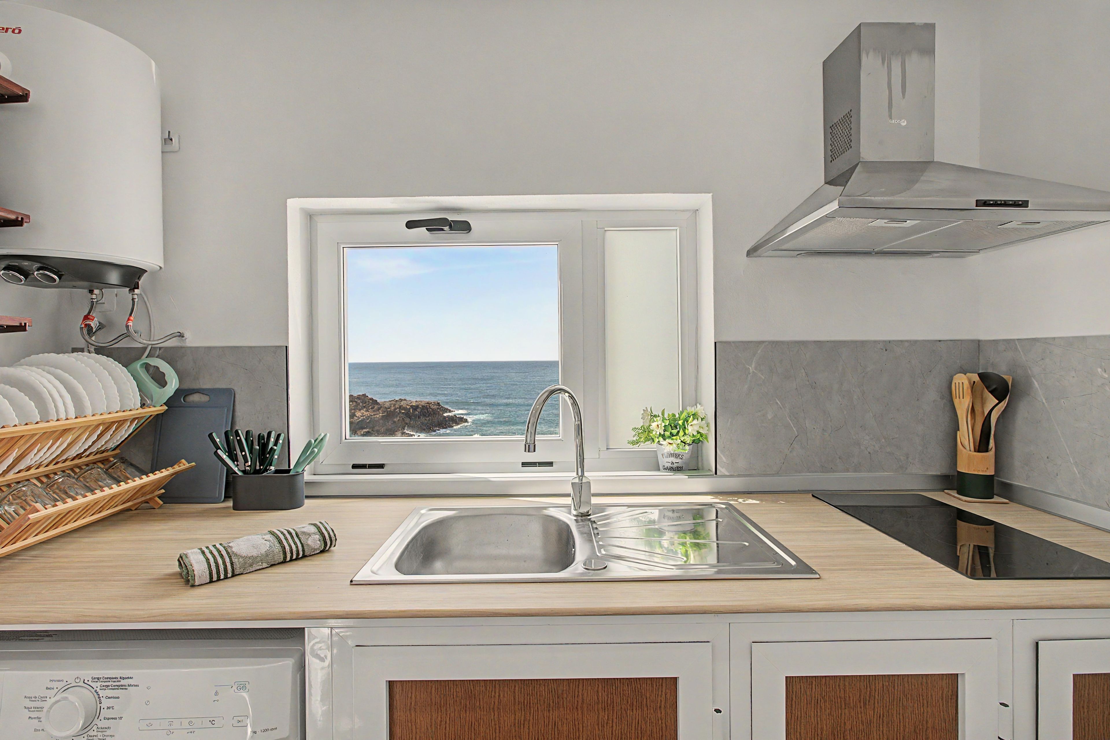 A kitchen with a view of the sea, a stainless steel sink, and wooden cabinets.