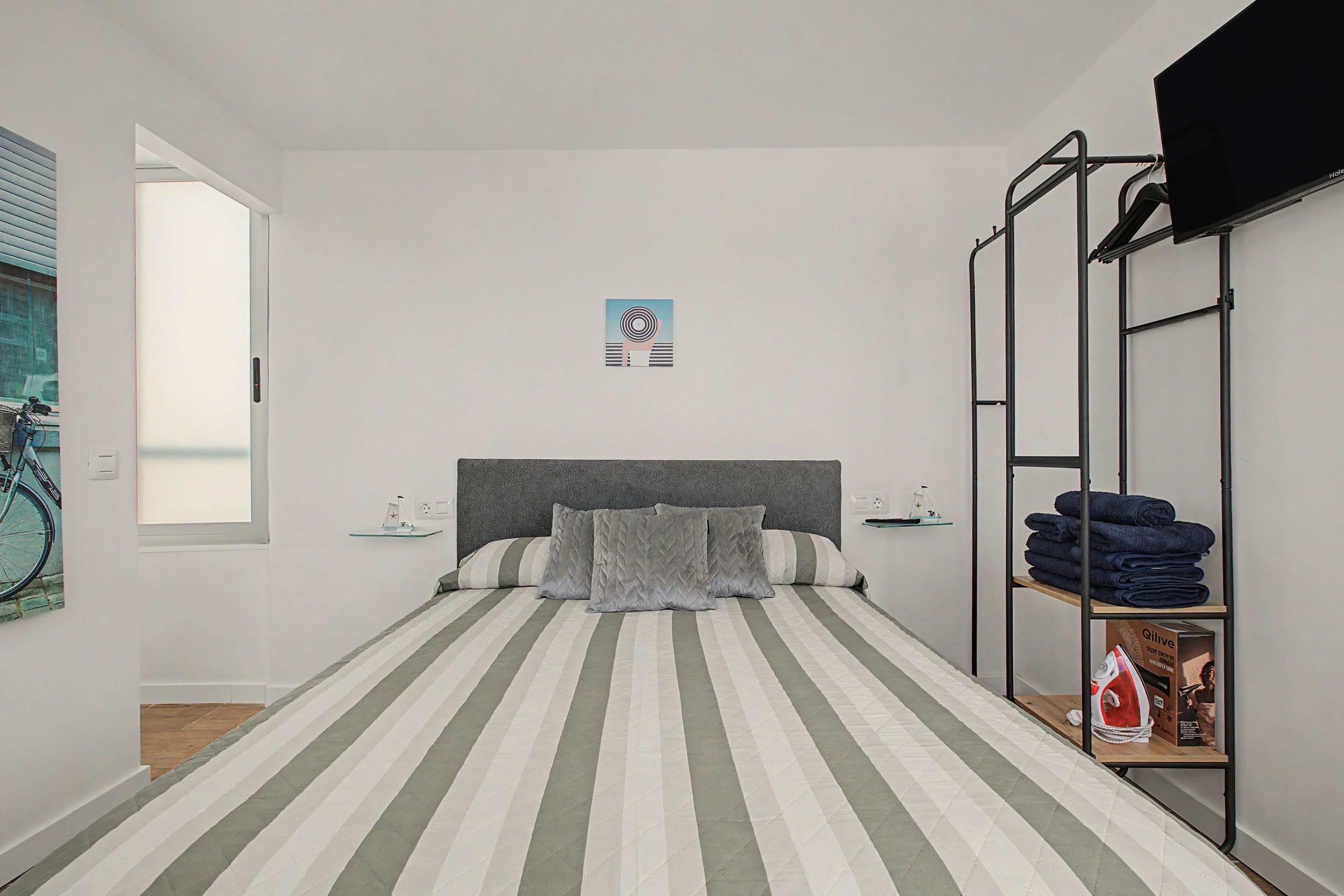 Une chambre avec un lit simple, une couvre-lit à rayures, une tête de lit et une étagère avec des serviettes pliées.
