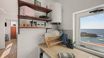 A kitchen with wooden shelves, a coffee machine, and a view of the sea through a window.