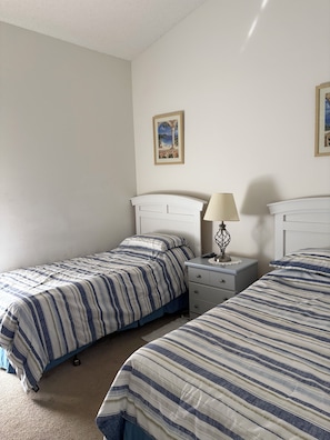 Un dormitorio con dos camas individuales, una mesita de noche con lámpara y una cómoda pequeña.