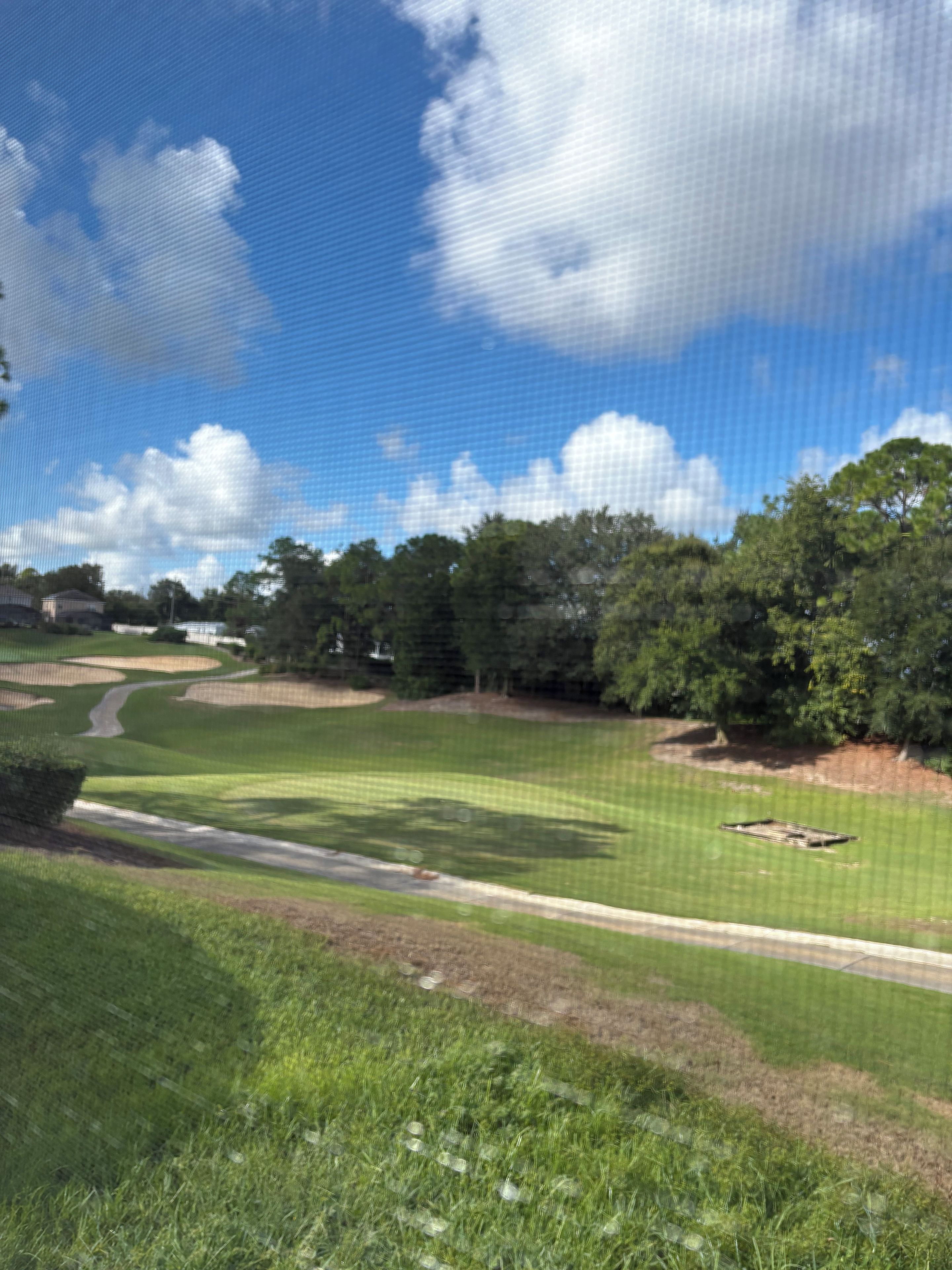 A golf course with a clear sky, trees, and a well-maintained lawn.