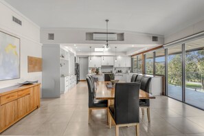 A modern kitchen with white cabinets, a dining area with a wooden table and black chairs, and large windows offering a view of the outdoors.