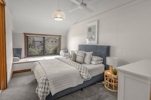 A bedroom with a bed, a window, a ceiling fan, and a wall-mounted artwork.