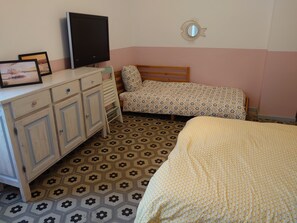 A bedroom with a bed, a desk, a television, and a patterned floor.