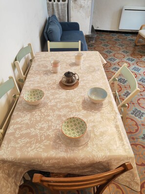 A dining table with a floral tablecloth, surrounded by wooden chairs, with a coffee pot and bowls on the table. - Entire Rental: Townhouse - La Palme, France (La Palme)