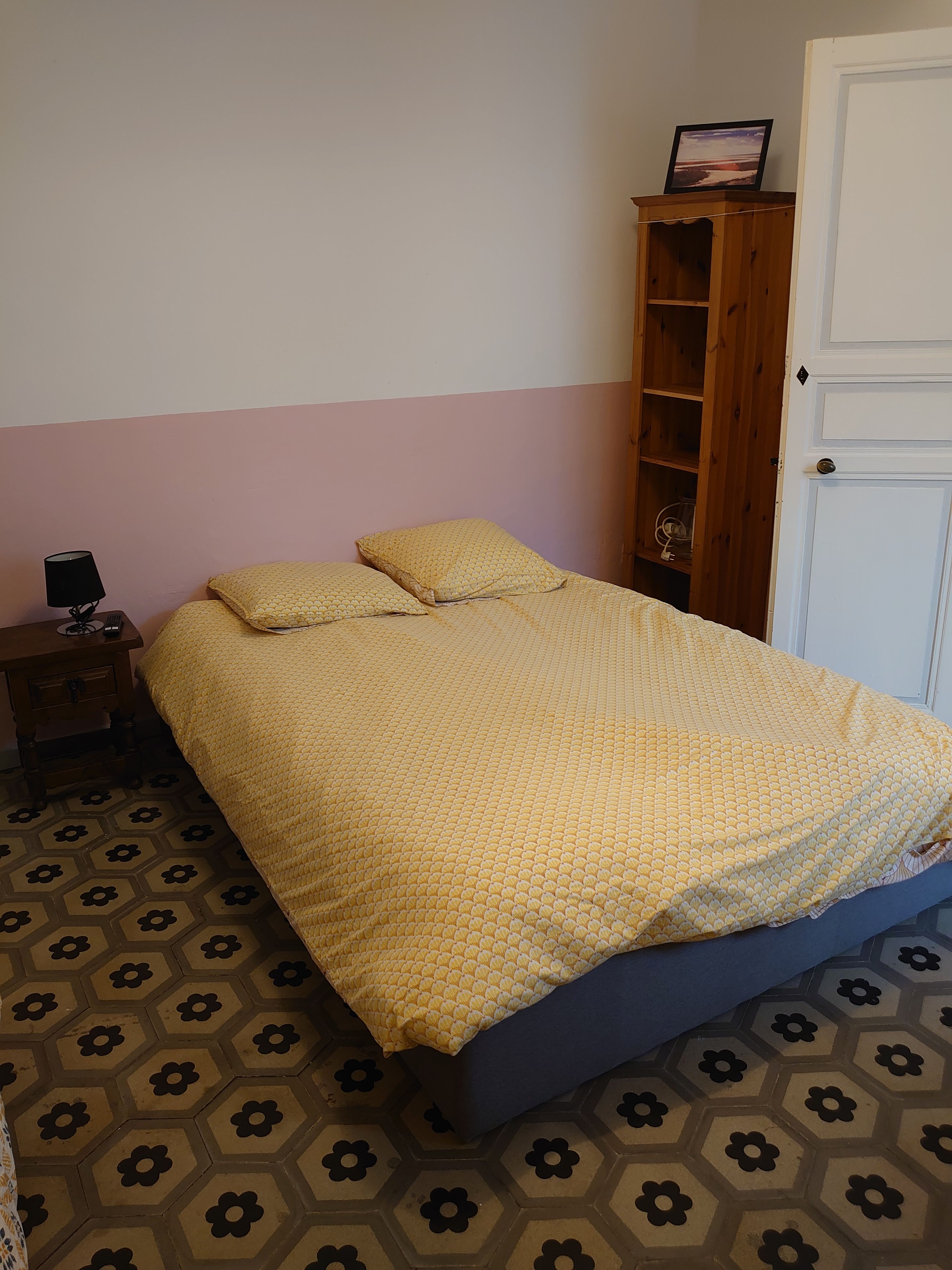 Una cama con una colcha estampada, una mesita de noche con una lámpara, un armario de madera y una puerta.