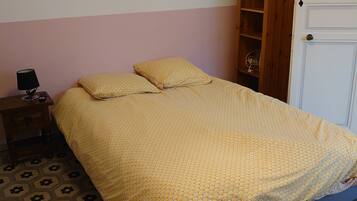 Una cama con una colcha estampada, una mesita de noche con una lámpara, un armario de madera y una puerta.