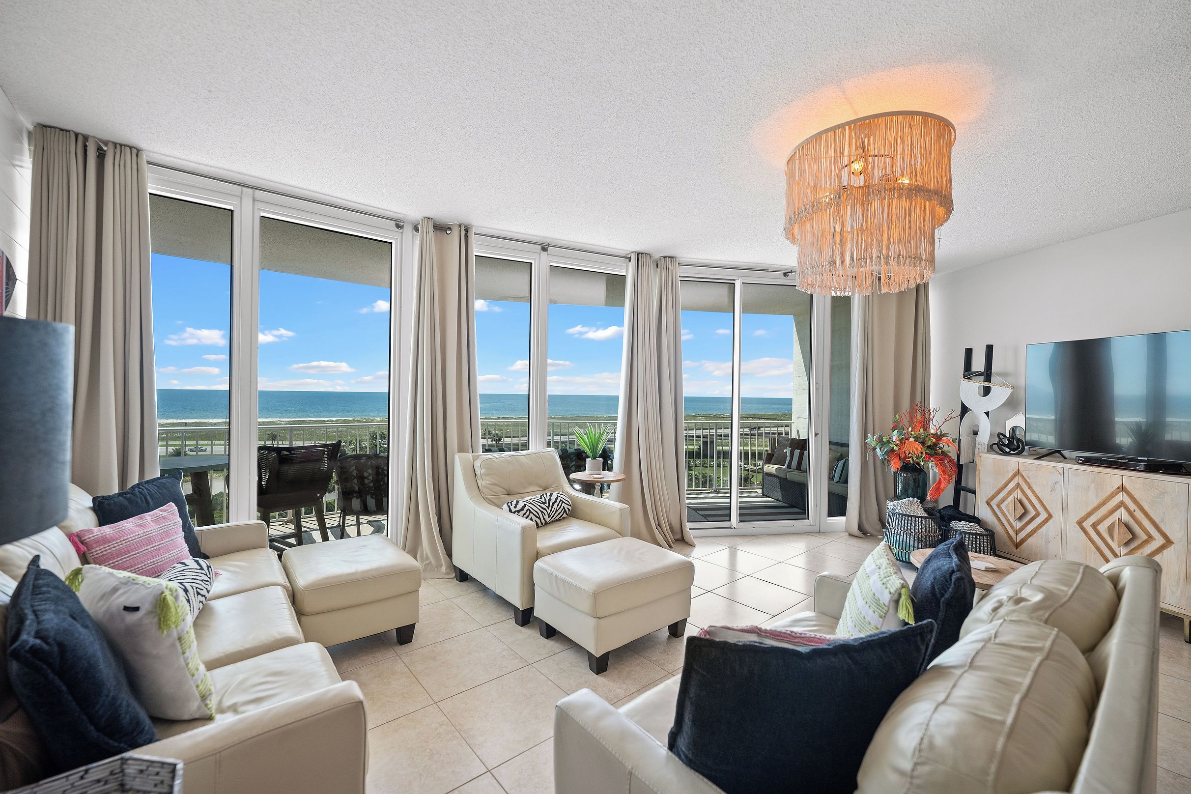 A spacious living room with a large TV, comfortable seating, and a view of the ocean.