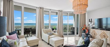 A spacious living room with a large TV, comfortable seating, and a view of the ocean.
