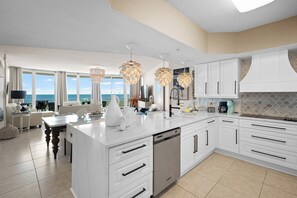 A modern kitchen with white cabinetry, a central island, and a view of the ocean through large windows. - Caribe BldgB-Fully Updated-Great Gulf Views-Orange Beach-Signature Properties (Orange Beach)