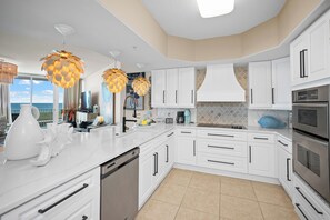 A modern kitchen with white cabinets, stainless steel appliances, and a view of the ocean. - Caribe BldgB-Fully Updated-Great Gulf Views-Orange Beach-Signature Properties (Orange Beach)