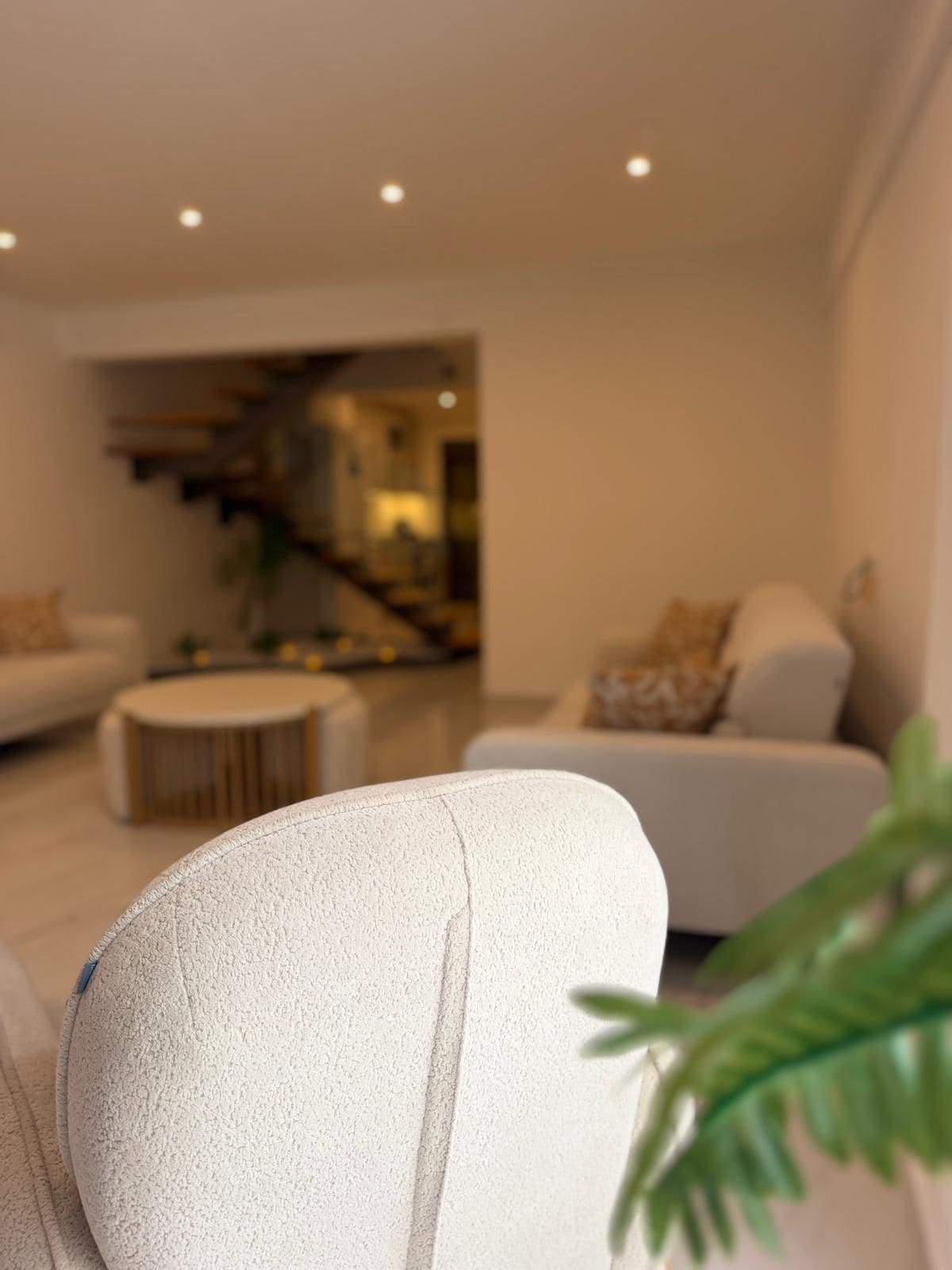 Uma sala de estar moderna com um sofá, uma mesa de centro redonda e uma escada que leva a um andar superior.