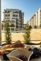 Un plato con pan tostado, aguacate y crema de chocolate, con una piscina y edificios al fondo.