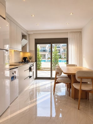 A modern kitchen with a dining area, a view of a swimming pool, and a balcony.