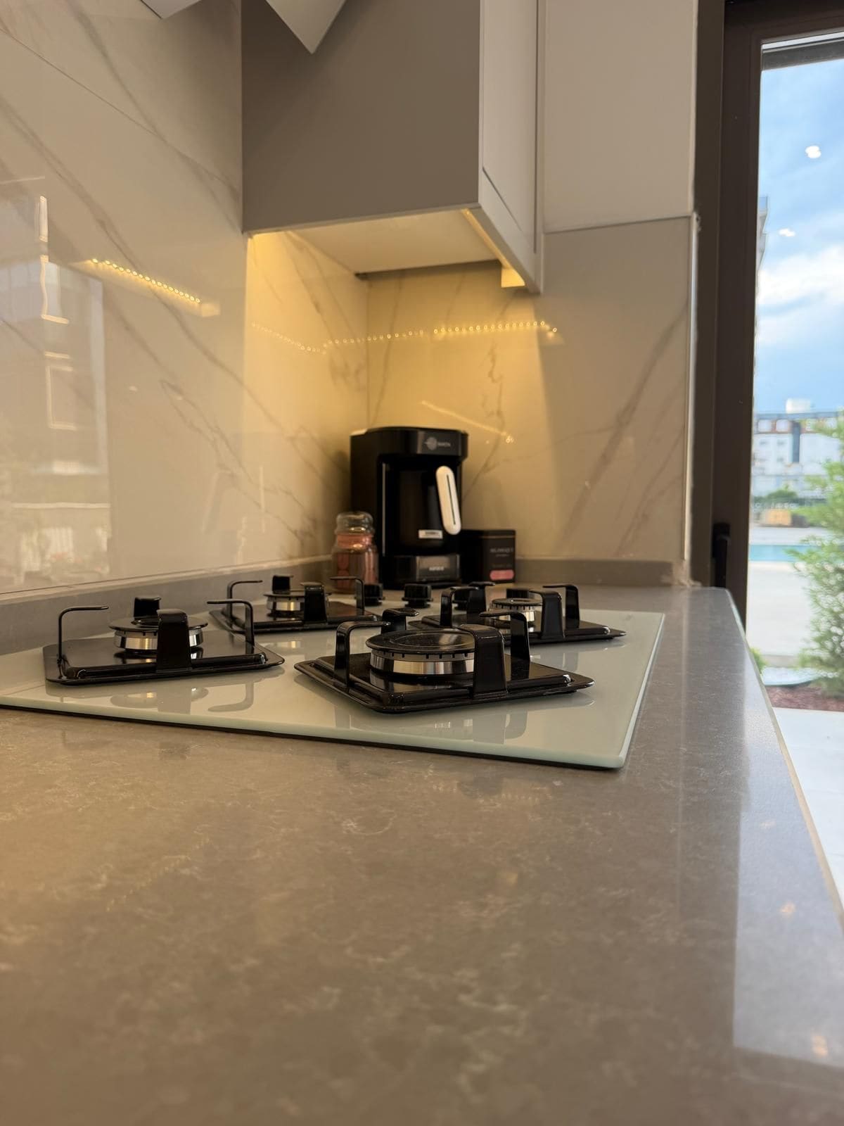 Uma cozinha com fogão moderno, cafeteira e vista para o exterior.