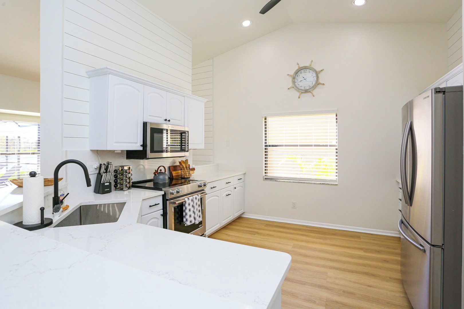 A modern kitchen with white cabinetry, stainless steel appliances, and a wooden floor.