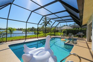 Ein Schwimmbecken mit Seeblick, umgeben von einer überdachten Terrasse mit Gartenmöbeln.
