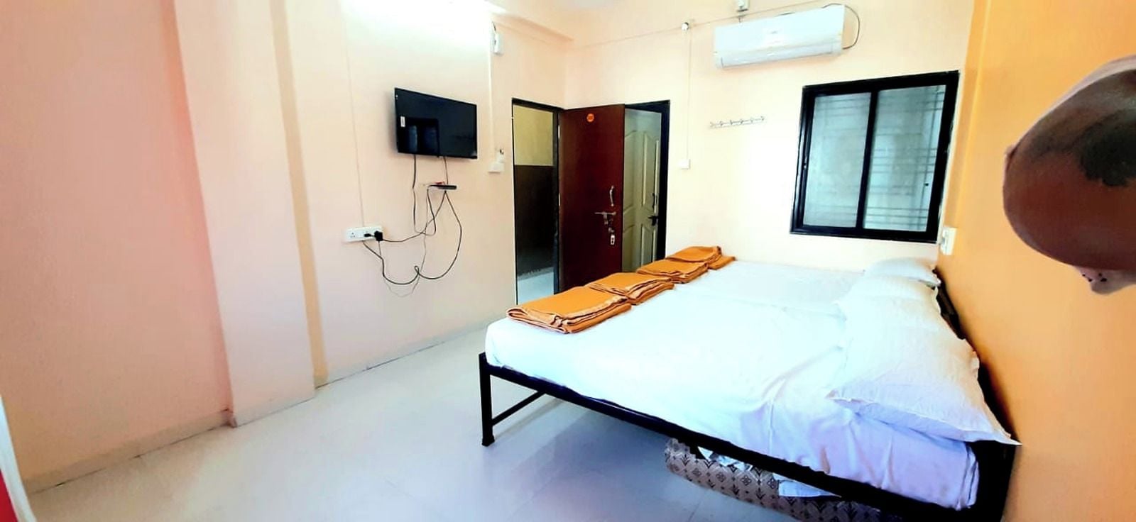A single-bed room with a bed, a wall-mounted TV, and a window.