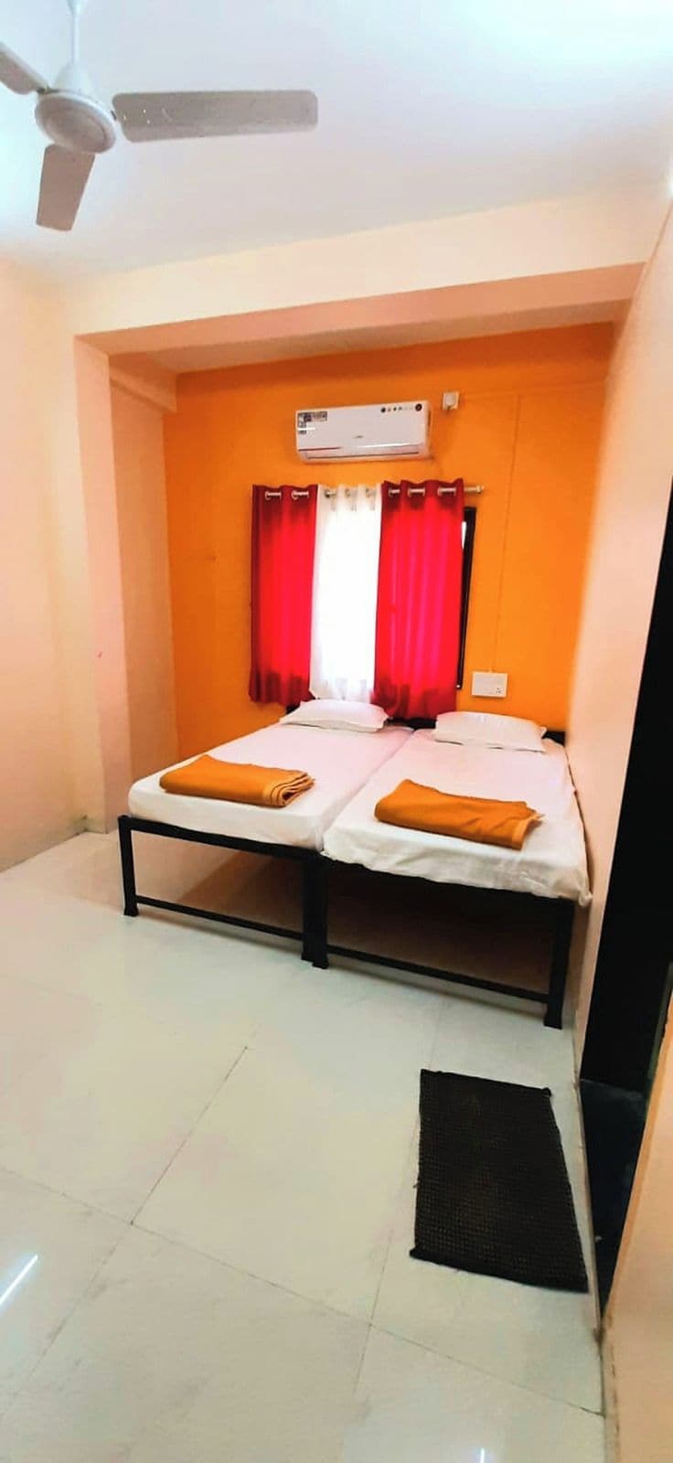 A room with two beds, a ceiling fan, an air conditioning unit, and a window with red curtains.