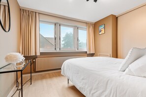 Ein Schlafzimmer mit einem Bett, einem Heizkörper, einem Fenster mit Vorhängen und einem Bild an der Wand.