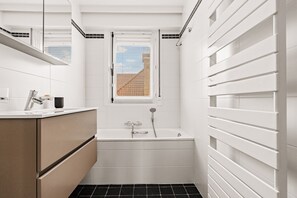 Ein modernes Badezimmer mit einer Badewanne, einem Waschbecken und einem Fenster mit Jalousien.