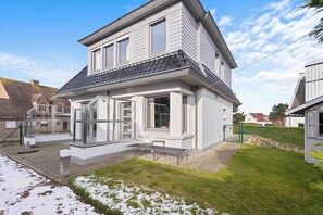 Ein zweistöckiges Haus mit großer Veranda, überdachtem Patio und gepflegtem Rasen.