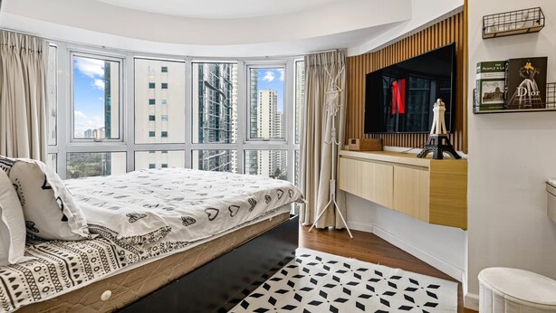 Une chambre moderne avec un lit, une grande fenêtre, une coiffeuse avec un miroir et une vue sur de hauts immeubles.