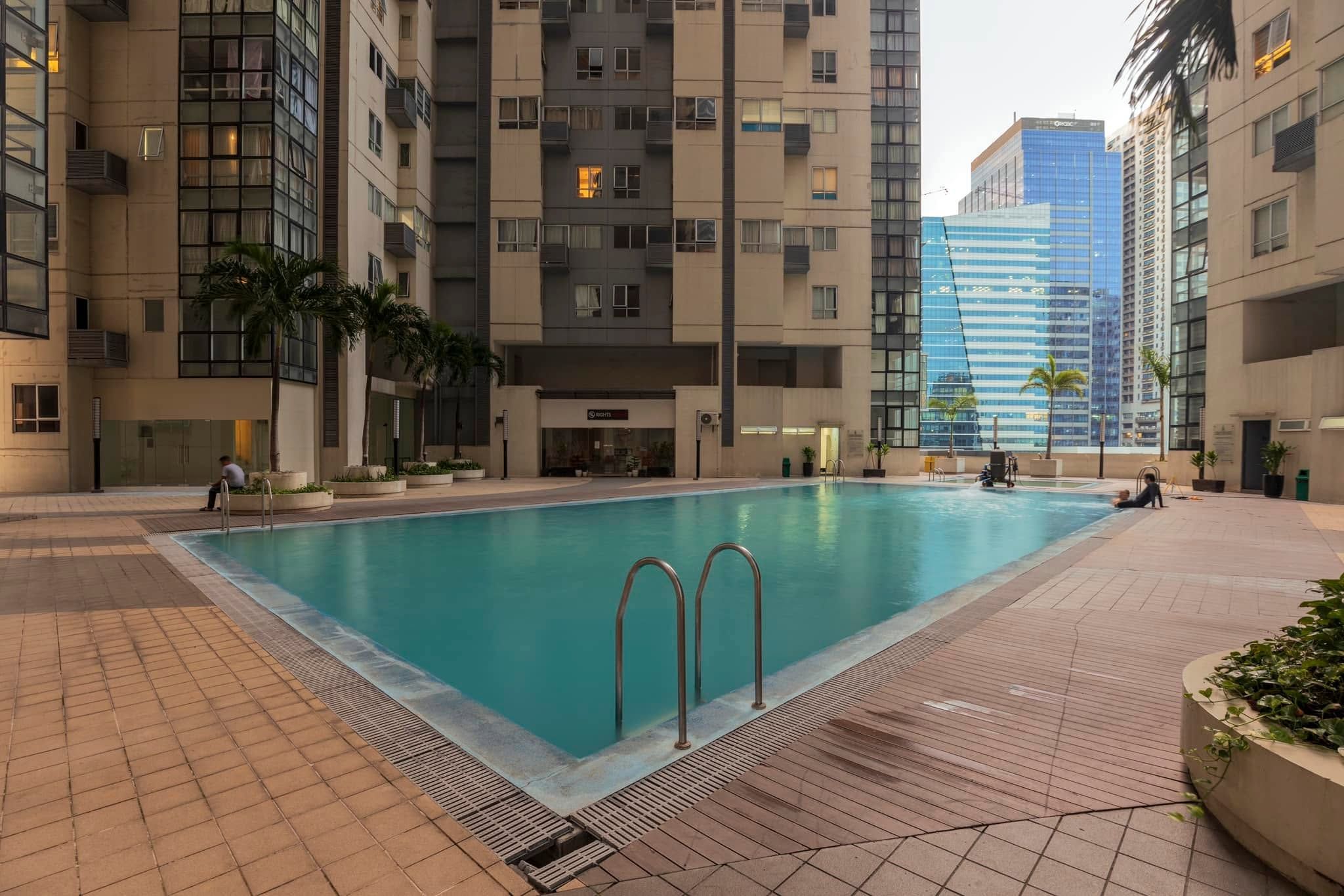 A swimming pool surrounded by high-rise buildings, with a few people around.