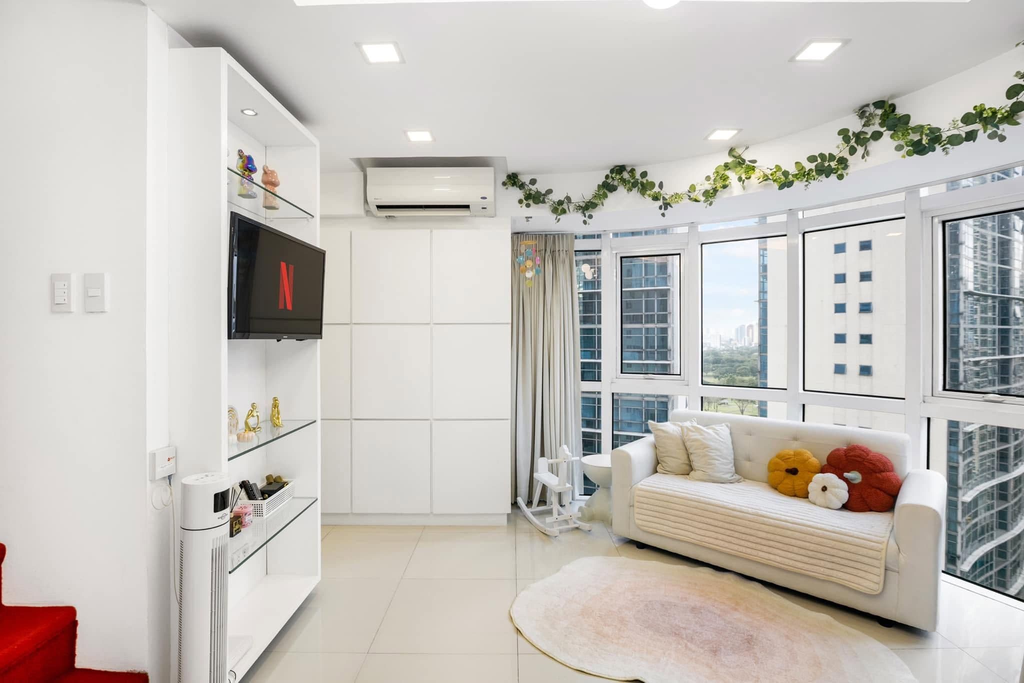 A modern living room with a white sofa, a flat-screen TV, and a large window with a city view.