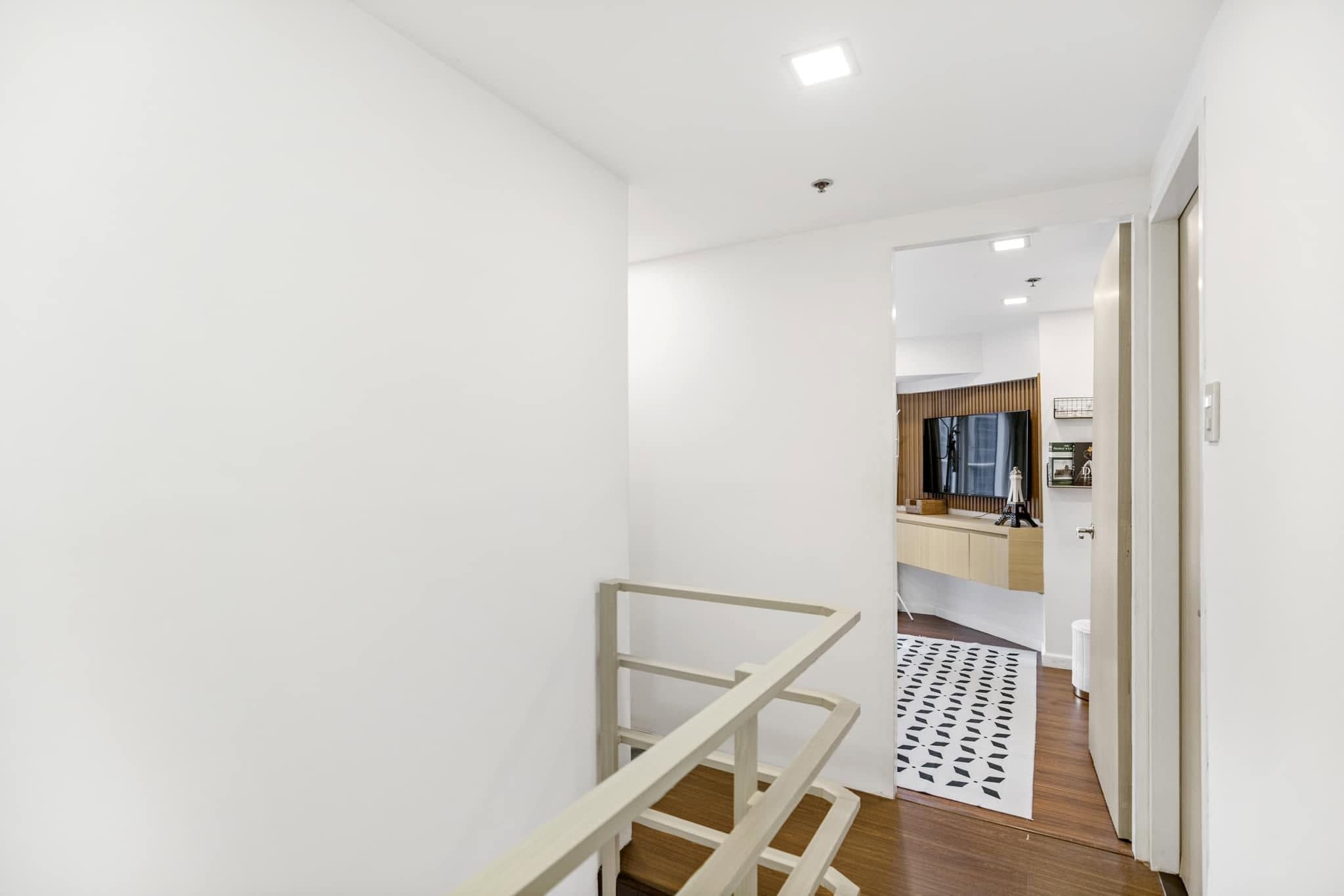 A modern interior with a staircase, a wooden floor, and a kitchen area visible through an open door.