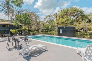 Ein Swimmingpool mit Liegestühlen und ein von Bäumen gesäumtes, umzäuntes Areal.