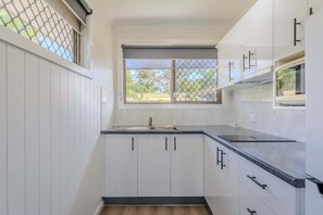 Een keuken met witte kasten, een zwart aanrecht en een raam met uitzicht op palmbomen.