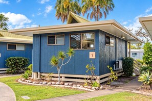 Een tweelaags huis met een blauwe gevel, een bord met het nummer '7' en een kleine tuin met verschillende planten.