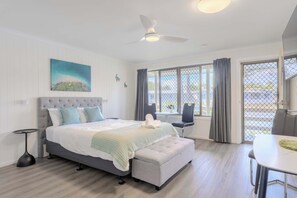 Ein Schlafzimmer mit einem Bett, einer Bank, einem Tisch und einem Fenster mit Vorhängen.
