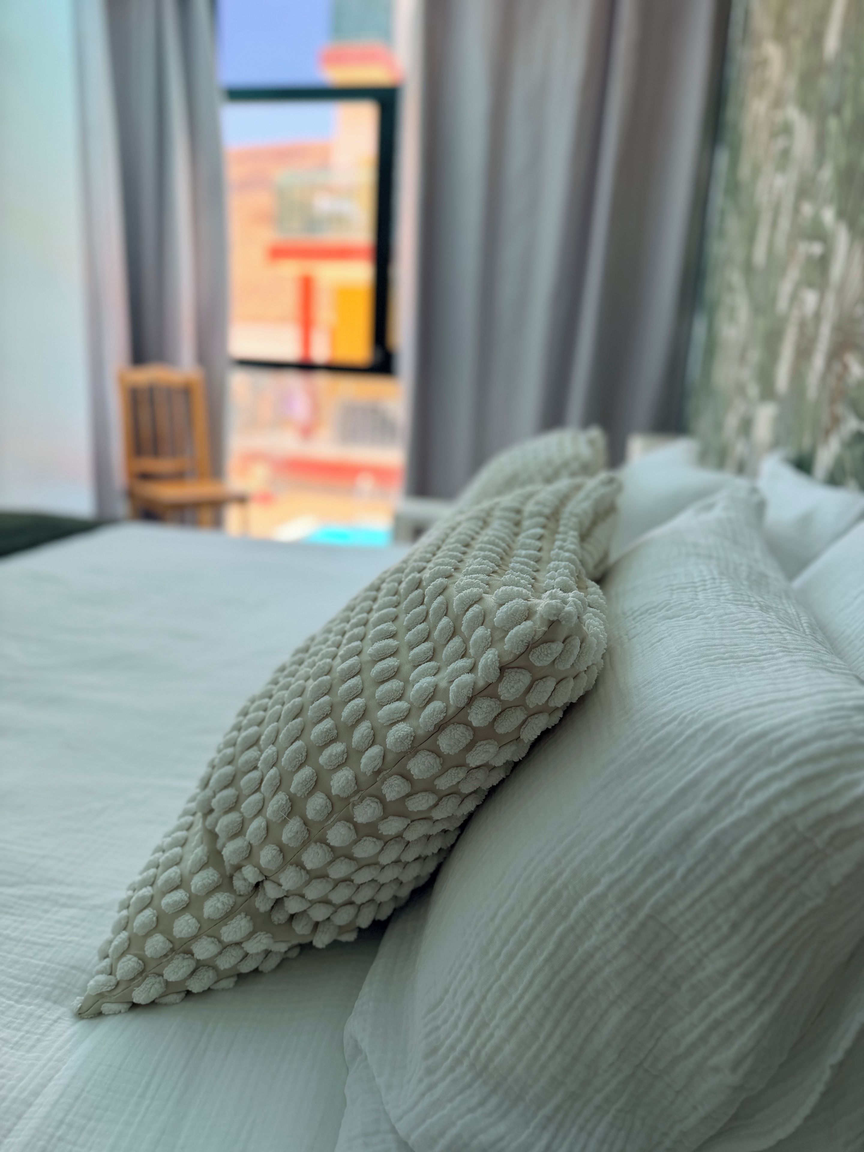 A bed with a textured pillow and a plain white bedspread.