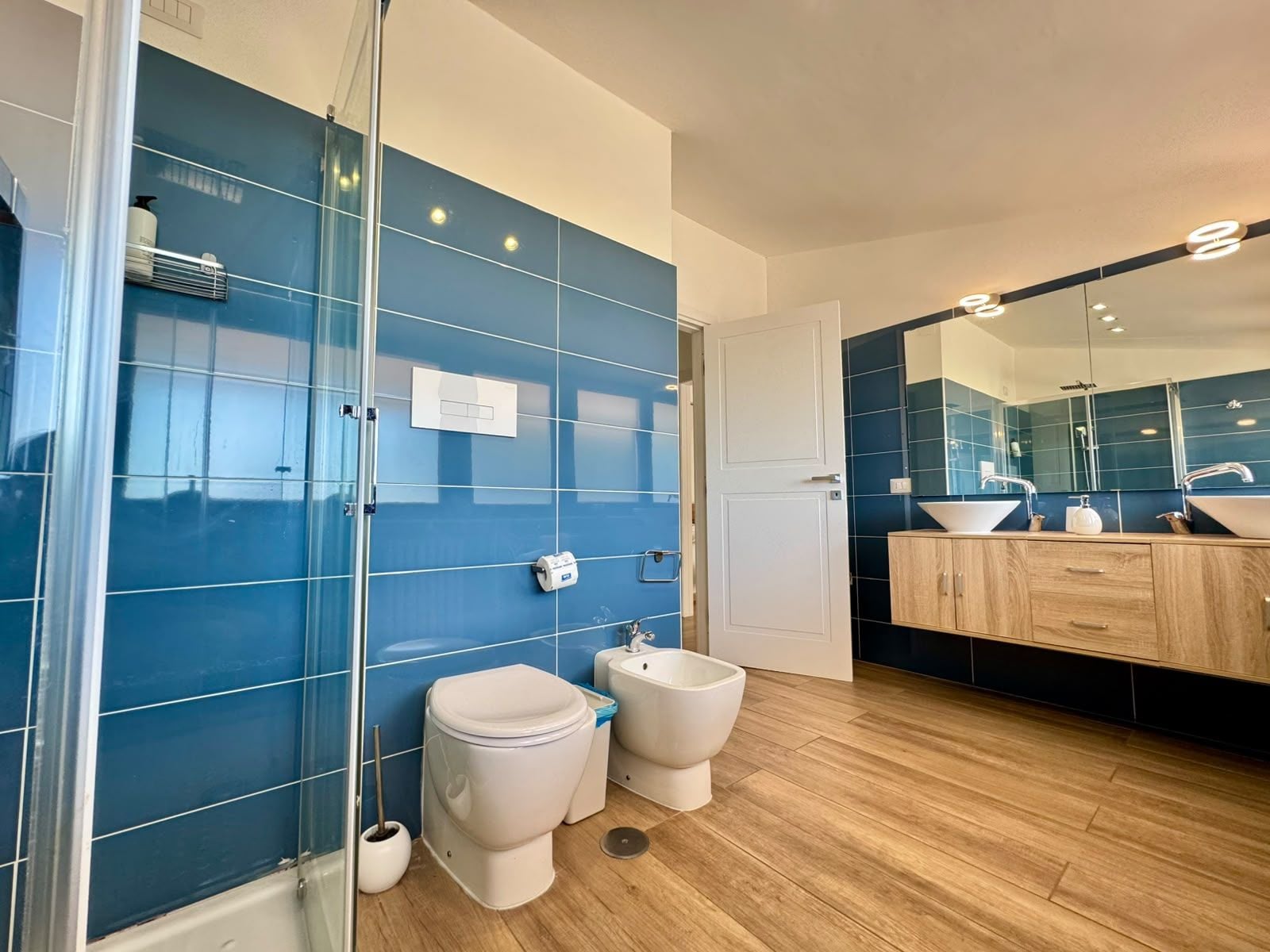 Ein modernes Badezimmer mit Duschkabine aus Glas, Toilette, Bidet und Waschtisch mit Spiegel.
