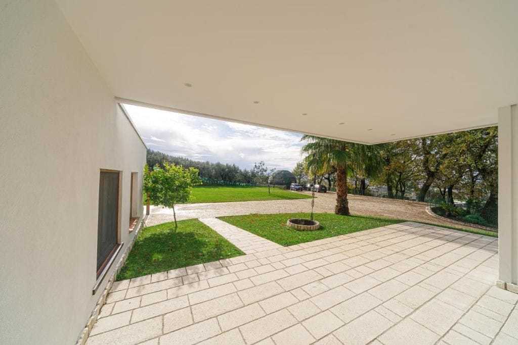 A modern building with a spacious patio area, a small lawn, and a view of a park with trees and a pathway.