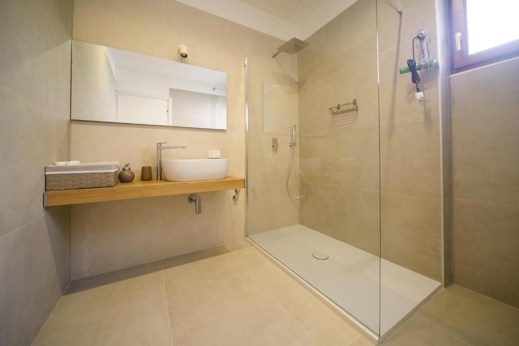 Ein modernes Badezimmer mit einer gläsernen Duschkabine, einem Holzwaschtisch mit weißem Becken und einem großen Spiegel darüber.