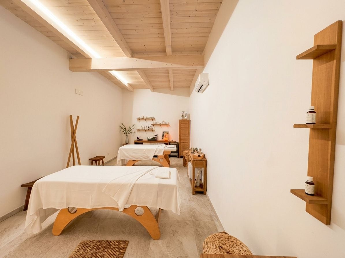 A spa room with two beds, wooden beams on the ceiling, and a shelf with bottles.