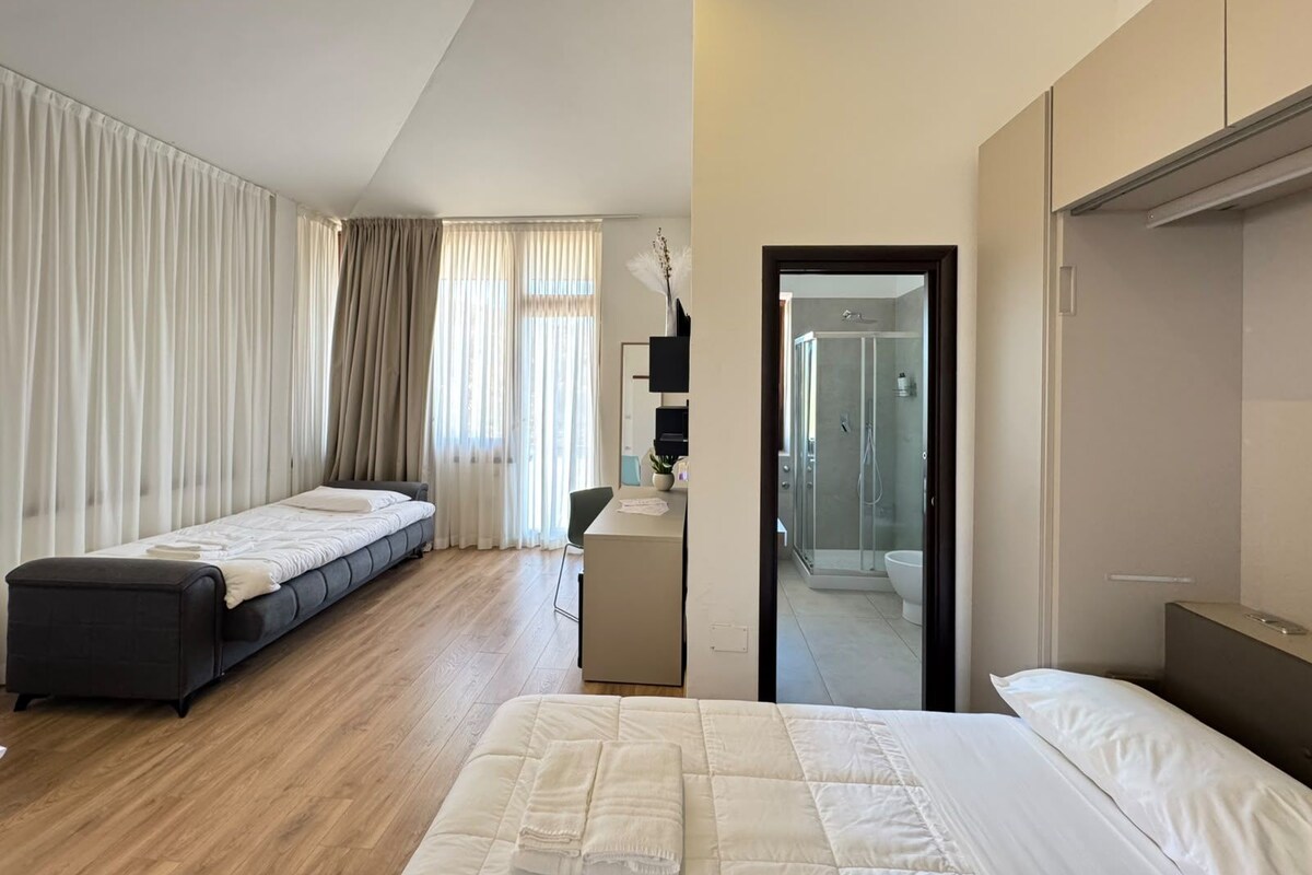Habitación de hotel con cama, escritorio, silla, armario y zona de ducha.