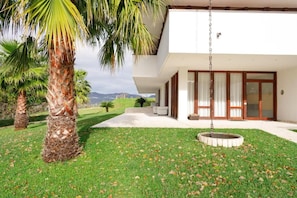 A modern two-story building with a flat roof, large windows, and a covered outdoor area with a circular seating area.