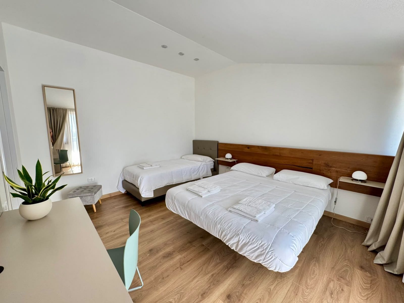 Ein Hotelzimmer mit einem großen Bett, zwei Nachttischen, einer Nachttischlampe, einem Sessel, einem kleinen Tisch und einer Zimmerpflanze.
