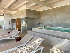 Un área de spa moderna con piscina, tumbonas y una pared de piedra.