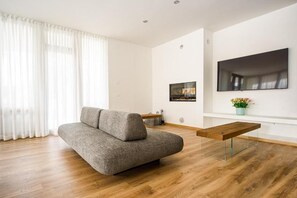 A modern living room with a grey sofa, a wooden coffee table, and a flat-screen TV mounted on the wall.