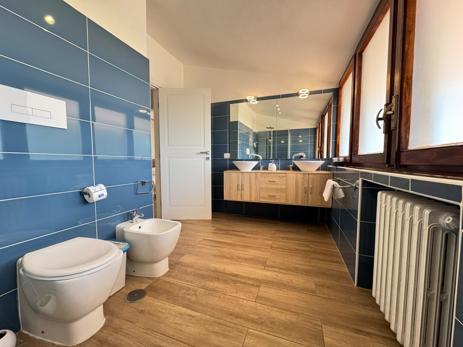 A modern bathroom with a bidet, two sinks, a mirror, and a radiator.